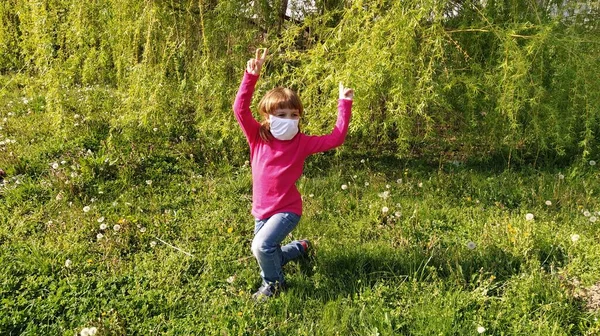 女の子6長い袖フクシアやホットピンクで歳 子供は白い保護外科用マスクを身に着けている 空気感染症の予防 女の子は踊っている 緑の草としだれ柳の葉 — ストック写真