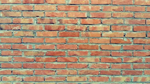 Old brickwork. Wall of an old residential building. Sunny evening lighting. Warm brown, red, orange, beige, yellow colors. Hardened cement is visible. Destruction on the stone from time and moisture.