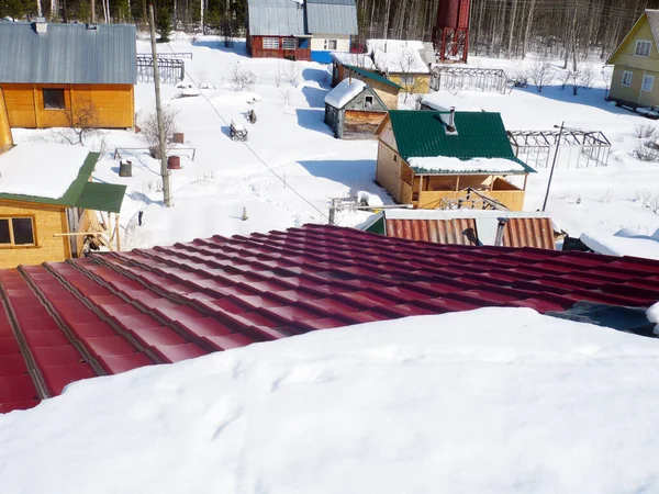 Summer house cooperative, top view, new red metal roof. Sunny winter day in the village. Photograph taken while standing on the roof. Snow and trees. Wooden little houses. DIY repair. — Stock Image Summer House Cooperative Top View New Red Metal Roof Sunny Royalty Free Stock Images
