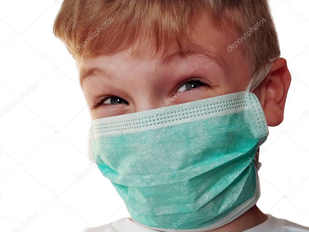 Face of a handsome white old boy in a green protective surgical mask. Tricky gray eyes. The child grimaces under a mask, squints his eyes and smiles. Blonde hair. White background. Isolate Effective virus protection