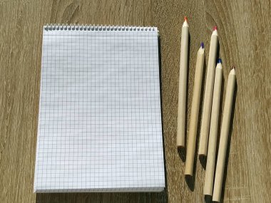 Boş defterin en üst görüntüsü ve tahta arka plandaki kalemler. Ofis kırtasiyesi. Öğrenci için okul malzemeleri. Eğitim konsepti. Boş kareli kağıt levha. Beş renkli kalem.