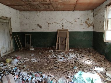 Terk edilmiş evin içinde. Grunge sahnesi. Yere saçılmış çöp. Duvarlarda yeşil boya var. Beyaz yarım duvar. Ahşap pencere çerçevelerine ateş etmiş. Şişeler, kağıt parçaları ve diğer eşyalar..