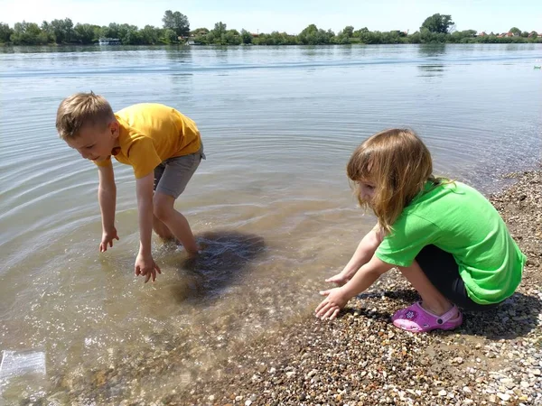 A boy and a girl are playing with plastic trash floating in the river. The concept of ecology and environmental protection. Plastic packaging and bottles float in the river. Serbia, Sava River.