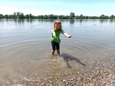 Kız dizine kadar suyun içinde duruyor ve kollarını öne doğru açıyor. Gölette bir çocuk. Uzun beyaz saçlı, gülümseyen, damla damla oynayan bir kız. Sırbistan, Sava Nehri ve Sremska Mitrovica.