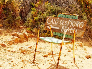 Calo des Moro beach hand written sign on a rusty chair showing direction to the most popular beach of Mallorca clipart