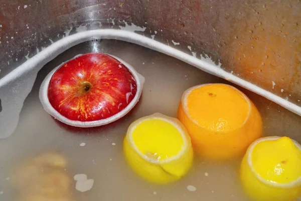 Elma, limon ve portakallar lavaboda deterjan ile sabunlu suda yüzüyor.