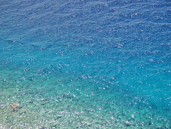 Turkuaz yarı şeffaf Hırvat denizi. Sığ su ve altında çakıl taşları var. Su üzerinde de ışıltılar var.