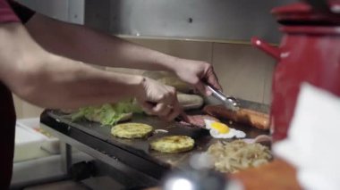 Aşçı hamburger, sosis, soğan ve yumurta pişiriyor.