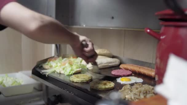 シェフの料理のハンバーガー ソーセージ 玉ねぎ ホットプレート上の卵 — ストック動画