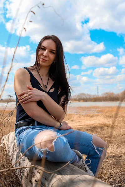 Uma Linda Garota Está Sentada Tronco Margem Rio Jeans Uma — Fotografia de Stock