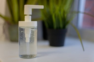 Bir şişe antibakteriyel sıvı, arka plandaki çiçeklere karşı pencerenin kenarında duruyor. Sıvı virüslere, bakterilere, mantarlara karşı.