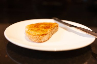 Beyaz ekmek hamurlu tost, tereyağı, gümüş bıçaklı beyaz tabak ve siyah granit tezgah.