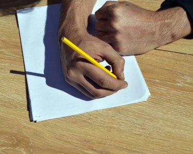 Bir adamın eli beyaz bir kağıda kurşun kalemle yazar.