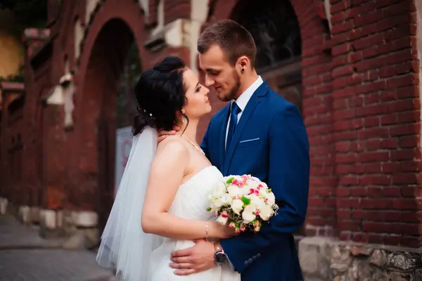 Feliz recém-casados beijando em uma parede vermelha — Fotografia de Stock