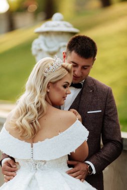 Gelin ve damat parkta birlikte yürürler. Beyaz elbiseli çekici gelin, damat koyu renkli şık bir takım giyiyor.