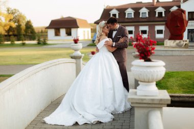 Gelin ve damat parkta birlikte yürürler. Beyaz elbiseli çekici gelin, damat koyu renkli şık bir takım giyiyor.