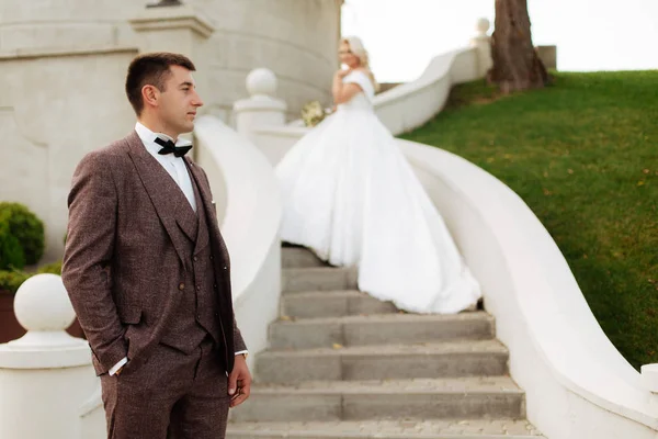 Gehen Braut und Bräutigam gemeinsam durch den Park. Charmante Braut im weißen Kleid, der Bräutigam trägt einen dunklen eleganten Anzug — Stockfoto