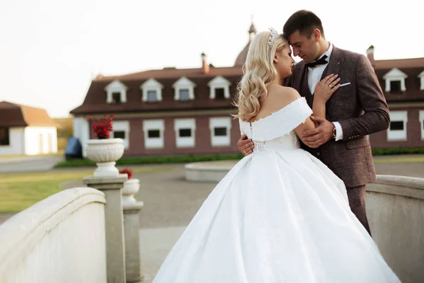 La novia y el novio caminan juntos en el parque. Encantadora novia en un vestido blanco, el novio está vestido con un traje elegante oscuro — Foto de Stock