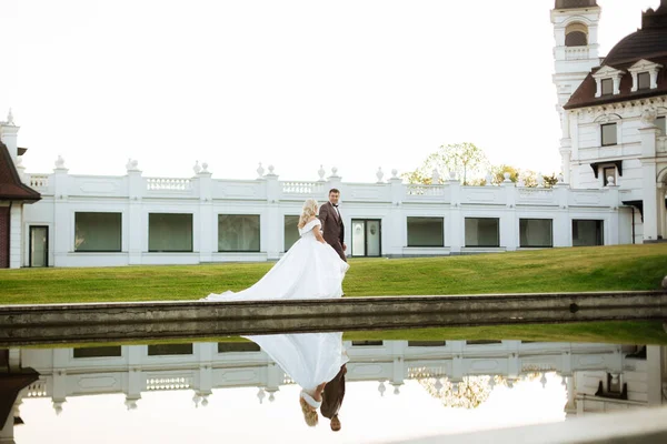 A menyasszony és a vőlegény együtt sétálnak a parkban. Elbűvölő menyasszony fehér ruhában, a vőlegény sötét elegáns öltönyben van. — Stock Fotó