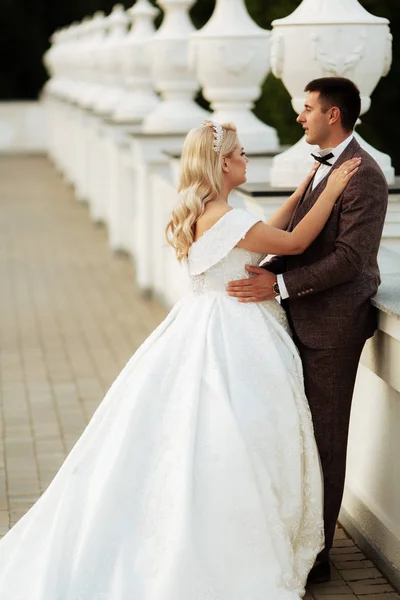 The bride and groom walk together in the park. Charming bride in a white dress, the groom is dressed in a dark elegant suit