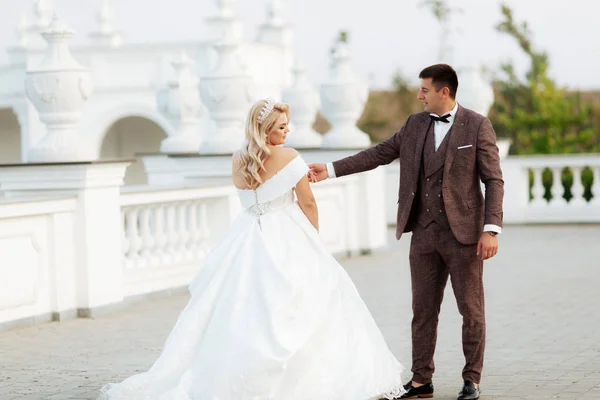 The bride and groom walk together in the park. Charming bride in a white dress, the groom is dressed in a dark elegant suit