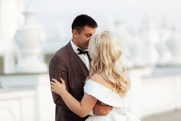 The bride and groom walk together in the park. Charming bride in a white dress, the groom is dressed in a dark elegant suit