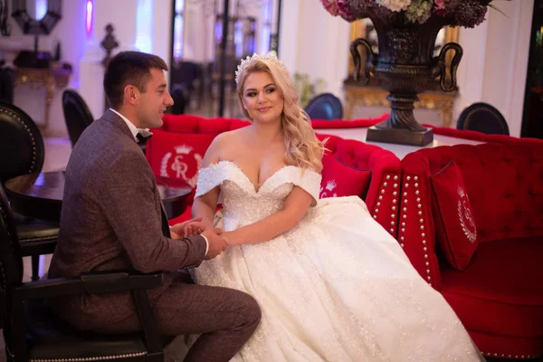 Novia y novio jóvenes en un café. El marido y la mujer se toman de la mano. Pareja cariñosa en un restaurante. Bonita novia y elegante novio. Día de la boda. Matrimonio . — Foto de Stock