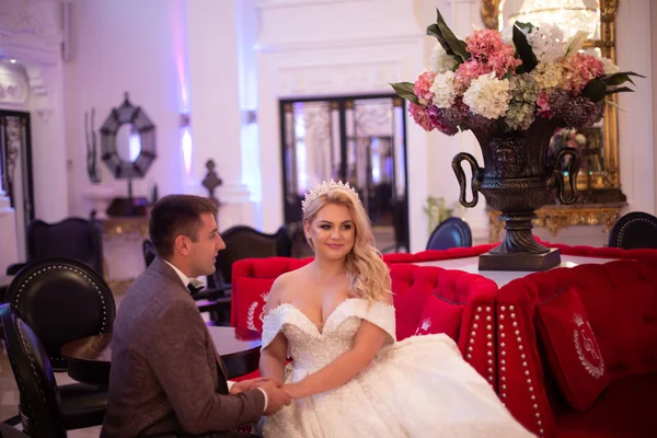 Young bride and groom in a cafe. Husband and wife hold each other's hands. Loving couple in a restaurant. Pretty bride and stylish groom. Wedding day. Marriage. — Stock Photo, Image