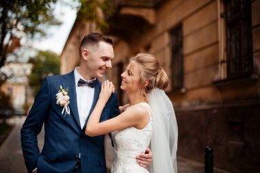 Fotoğraf çekim düğün. Gelin ve damat şehirde yürüyüş. Kucaklayan ve birbirine bakarak evli çift. Buket tutarak. Açık, tam vücut