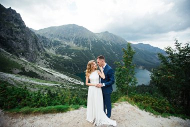 Dağlarda evlenen evli bir çift (gelin ve damat). Arka planda bir dağla gölün ortasında sarılmak.