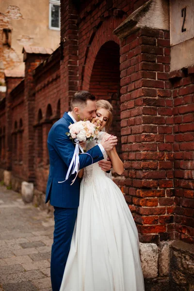 Casal de casamento lindo andando na cidade. Brilho em um terno elegante e noiva em um belo vestido branco, o casal está andando pelas ruas da cidade no dia do casamento. Juntos. Conceito de casamento — Fotografia de Stock