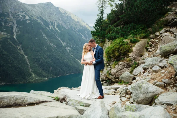 Bruden och brudgummen blundade och kramade varandra mot bakgrund av höga klippor och hav. — Stockfoto