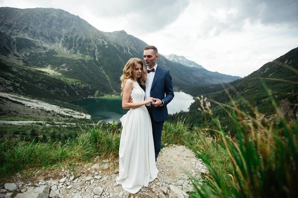 Nevěsta a ženich u jezera v horách. Pár pohromadě na pozadí horské krajiny. Jezero Morskie Oko. Tatranské hory v Polsku. — Stock fotografie