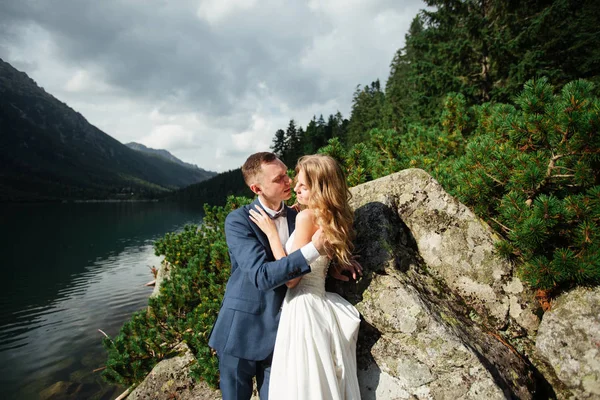 Bruden och brudgummen blundade och kramade varandra mot bakgrund av höga klippor och hav. — Stockfoto