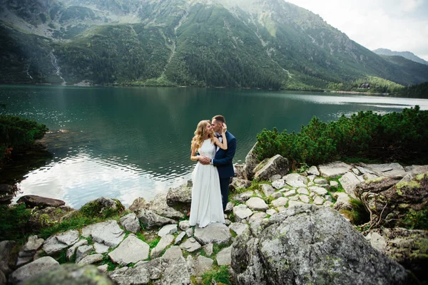 Bruden och brudgummen nära sjön i bergen. Ett par tillsammans mot bakgrund av ett bergslandskap. Morskie Okosjön. Tatrabergen i Polen. — Stockfoto