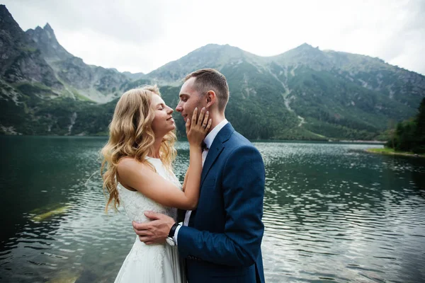 Bruden och brudgummen nära sjön i bergen. Ett par tillsammans mot bakgrund av ett bergslandskap. Morskie Okosjön. Tatrabergen i Polen. — Stockfoto