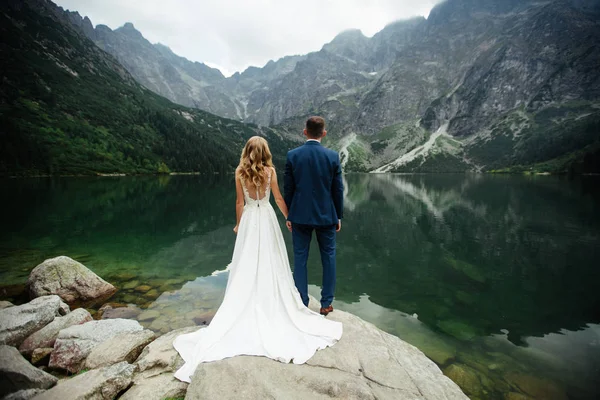 Bruden och brudgummen nära sjön i bergen. Ett par tillsammans mot bakgrund av ett bergslandskap. Morskie Okosjön. Tatrabergen i Polen. — Stockfoto