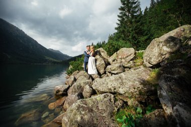 Polonya 'daki Sea Eye gölünün taşlı kıyısında duran şehvetli düğün çifti..
