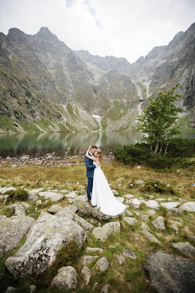 Krásný mladý svatební pár ženich a nevěsta stojící na zeleném svahu, kopec. Západ slunce v Karpat — Stock fotografie