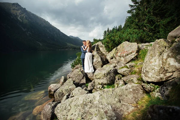 Getrouwd stel (bruid en bruidegom) trouwen in de bergen. knuffelen in het midden van een meer met een berg op de achtergrond — Stockfoto