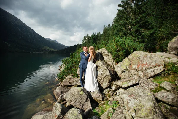 Vackert bröllopsfoto på Fjällsjö. Lycklig asiatisk par i kärlek, Brud i vit klänning och brudgummen i kostym är fotograferade mot bakgrund av den Kazakiska landskapet — Stockfoto