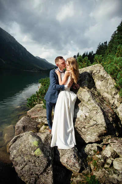 Bride with beautiful white dress and bride overlooking beautiful green mountains and lake with blue water — Stock Photo, Image