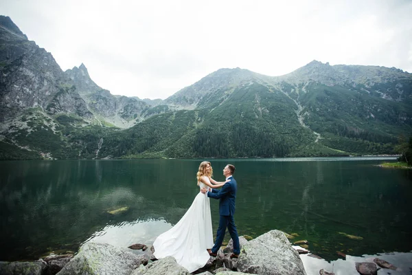 Gift par (brud och brudgum) gifta sig i bergen. kramas mitt i en sjö med ett berg i bakgrunden — Stockfoto