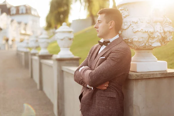 Retrato de estilo de vida del novio feliz posando para la cámara al aire libre en la naturaleza con roble en el fondo. Alegre prometido con la cara sonriente en jakcet, corbata y camisa blanca retrato antes de la ceremonia de boda — Foto de Stock