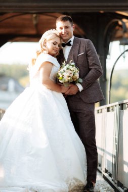 Gelin ve damat parkta birlikte yürürler. Beyaz elbiseli çekici gelin, damat koyu renkli şık bir takım giyiyor..