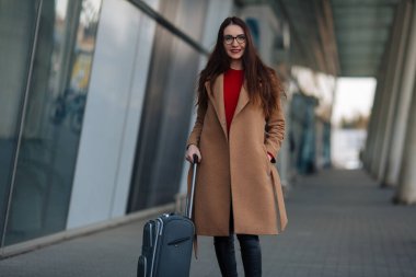 Gülümseyen başarılı iş adamının uzun bir portresi havaalanında bavulu çekiyor..