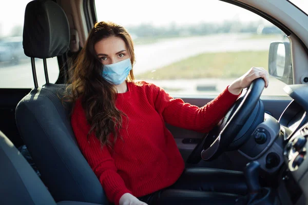 Coronavirus maskeli genç bir kadın arabada oturuyor..
