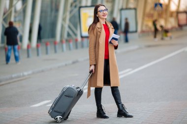 Gülümseyen başarılı iş adamının uzun bir portresi havaalanında bavulu çekiyor..