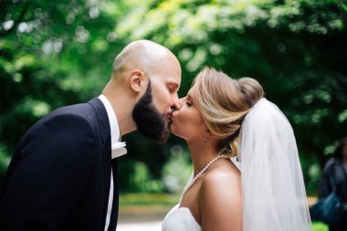 Genç ve güzel bir gelin ve kocası bir buket çiçekle bir yaz parkında dikiliyor..