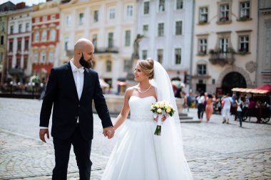 Genç ve güzel bir gelin ve kocası bir buket çiçekle bir yaz parkında dikiliyor..